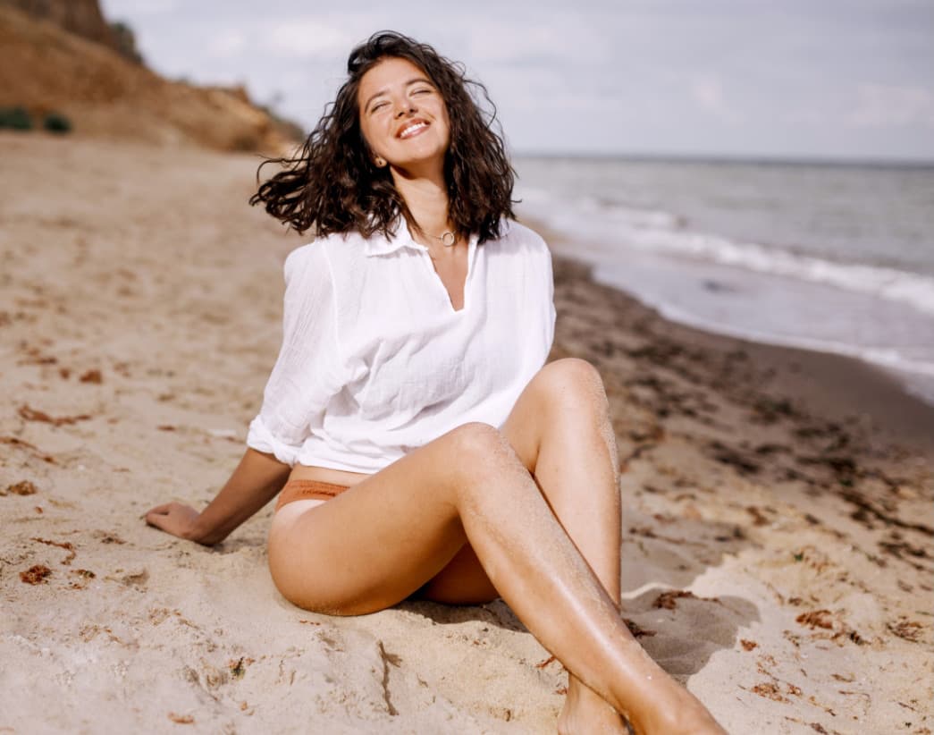 Woman sitting on beach wearing a white blouse