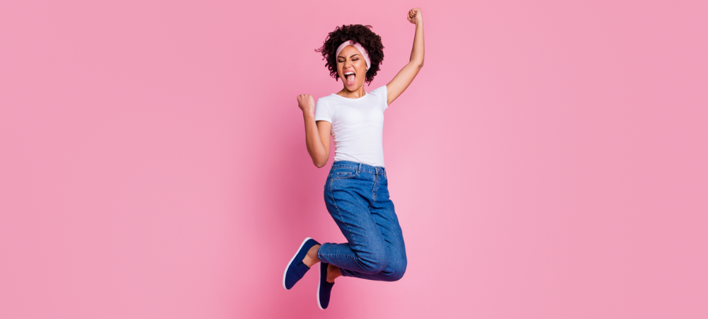 pretty african-american woman jumping for joy against pink backdrop