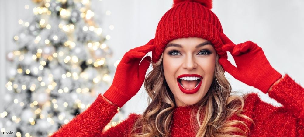 Happy woman in red hat gloves sweater standing in front of a Christmas tree 