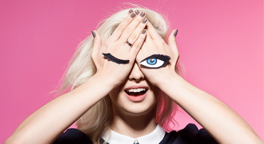 Woman with her hands over her eyes and paper illustration eyes stuck on her hands
