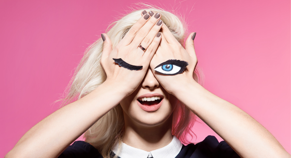 Woman covering her eyes with her hands which have a paper wink stuck to them.