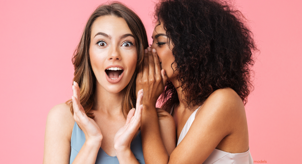 One woman whispering a secret to the other woman who looks surprised