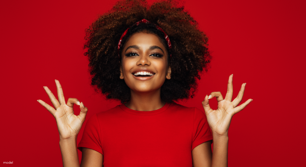 Beautiful African-American Woman wearing red, standing against a red backdrop, and hands in OK signs.