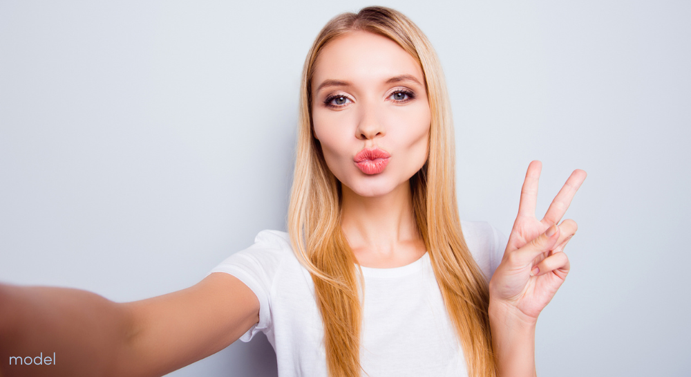 Pretty blonde looking at camera taking selfie flashing the peace sign with two fingers