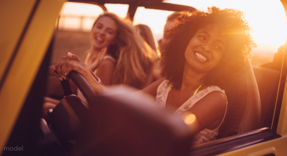 Smiling group of women driving in an open jeep at sunset 