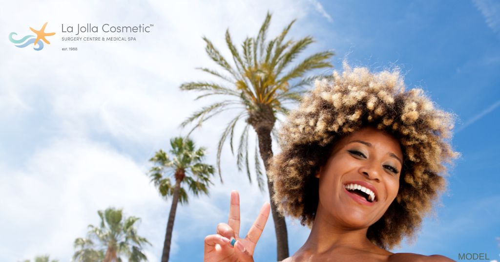 beautiful woman with curly hair taking a selfie in front of palm trees (model)