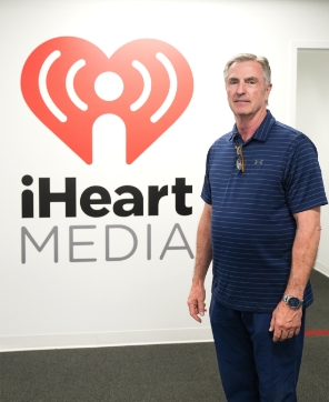 Dr. John Smoot standing in front of the iHeart Media logo