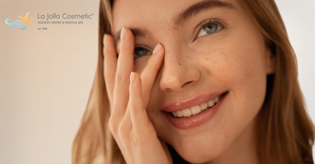 Woman with freckles on their face is holding her hand to their face (model)
