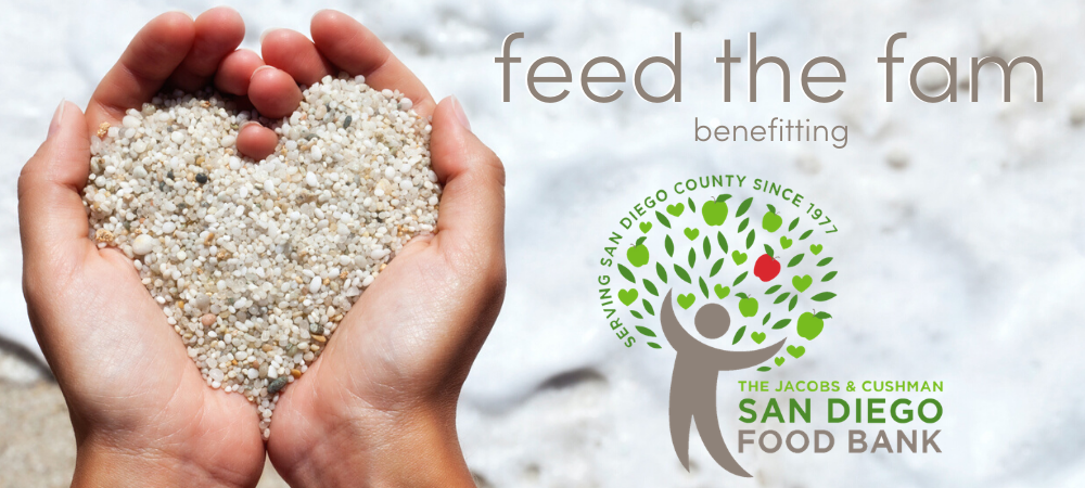 Hands holding small pebbles shaped into a heart on a beach, next to text reading “feed the fam benefitting” and the logo for The Jacobs & Cushman San Diego Food Bank.