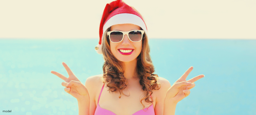 Woman in a pool leaning on the edge, pulling a Santa hat over her eyes and smiling